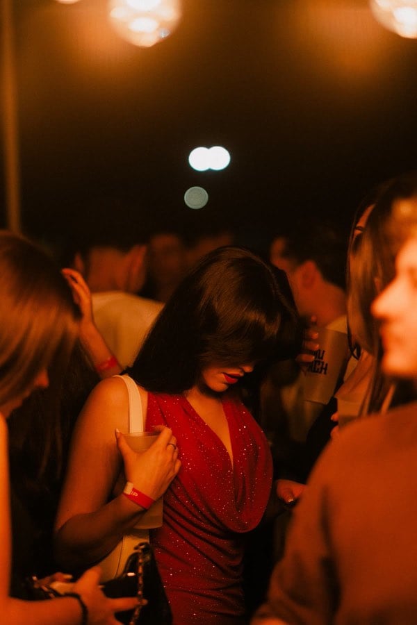 Woman in a red dress looking down beneath warm party lights