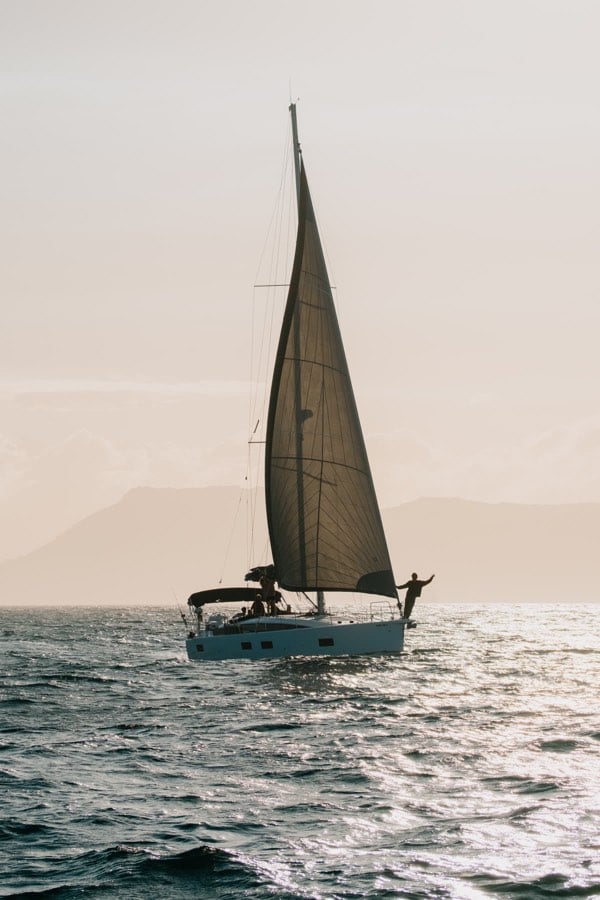 Man standing on a sailboat with the sea and distant mountains behind him