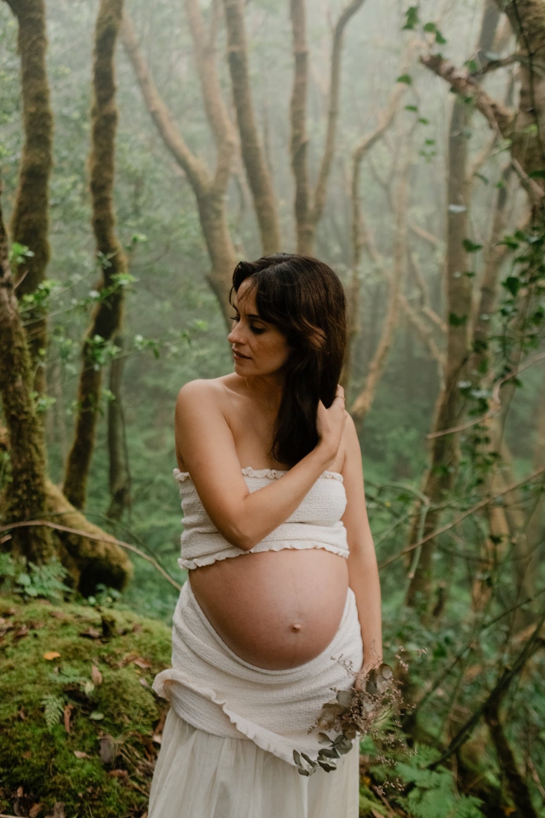 Pregnant woman in a white dress surrounded by a misty laurel forest